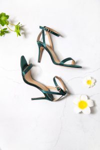 Stylish green heels on white backdrop with flowers, perfect for fashion showcases.