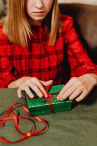 A young woman in red dress wraps a glittery green gift box with red ribbon, perfect for holiday themes.