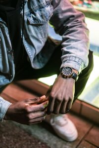 Close-up of a fashionable man crouching, showcasing wristwatch and denim jacket detail.