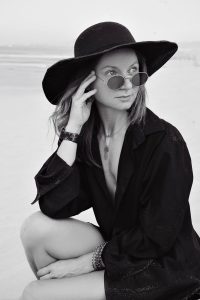Striking black and white portrait of a stylish woman in a hat on the beach.