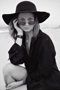 Stylish woman in black attire poses elegantly on a beach, exuding confidence and grace.