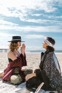 Women in boho attire meditate together on a serene beach.