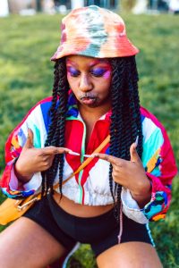 Colorful portrait of a woman in vibrant street style attire, showcasing bold makeup outdoors.