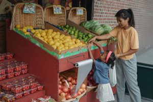 A mother and daughter selecting fresh produce at an outdoor fruit market.