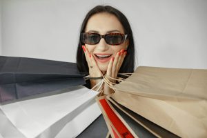 Smiling woman in sunglasses holding multiple paper shopping bags indoors.