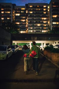 A couple walking together along a dimly-lit urban street at night.