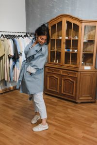 A woman tries on a blue trench coat in a stylish clothing store.