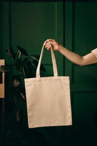Simple cotton tote bag held by a hand against a green background, ideal for eco themes.