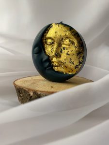 Elegant moon and sun face candle with gold leaf detail on a wooden slice, emphasizing art and symbolism.