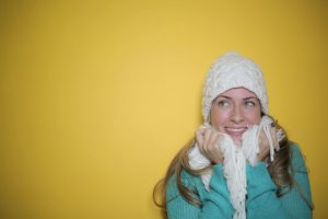 A woman in winter clothing smiles warmly against a vibrant yellow backdrop.