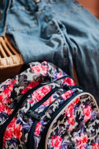 Close-up of a floral camouflage backpack with denim pants in the background.