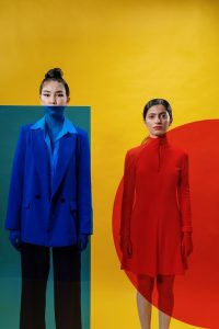 A striking studio image of two women in bold blue and red outfits against a vibrant yellow backdrop.