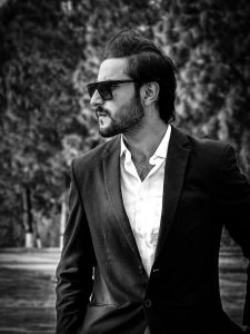 Black and white portrait of a man in a suit wearing sunglasses, set outdoors for a fashion-forward look.