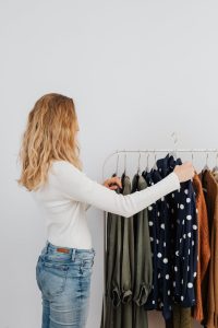 A woman with blond hair selecting clothes from a clothes rack indoors.