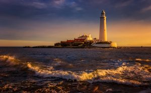 A mesmerizing view of St Mary's Lighthouse at sunset with waves crashing on the shore, located on the coast of England.