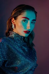 Striking portrait of a woman with colorful makeup and glitter attire, showcasing modern fashion and style.