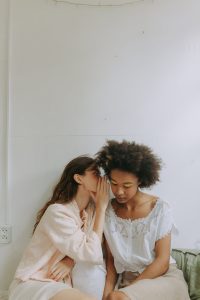 Two women seated indoors, whispering secrets in a calm and minimalist space.
