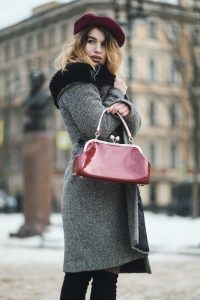 Stylish woman in winter coat and beret holding handbag outdoors.